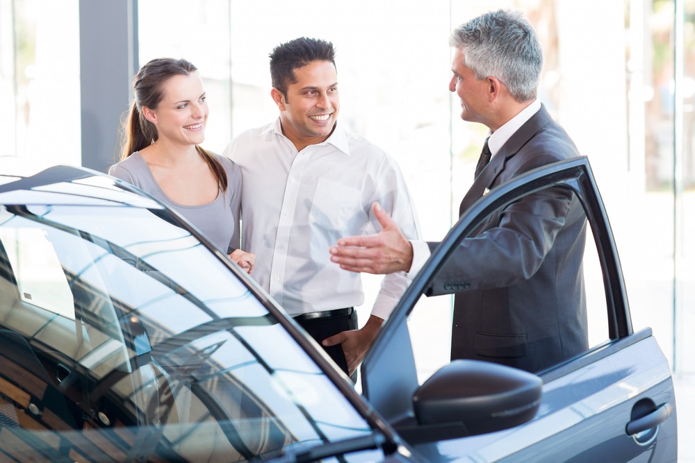 Car dealer showing couple a new car in showroom