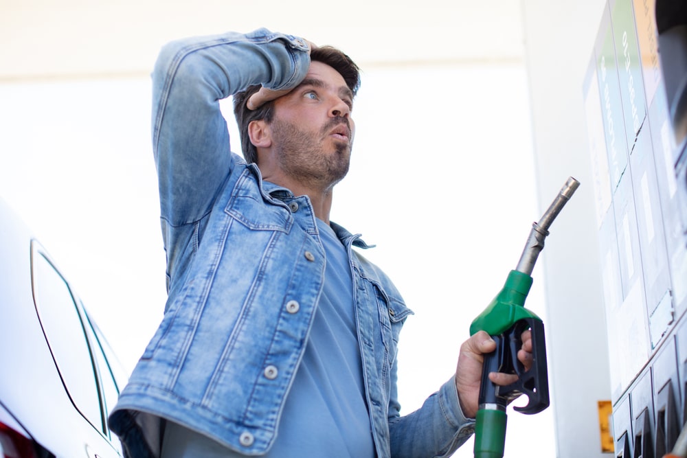 Man in denim jacket holding fuel pump at petrol bowser looks shocked at fuel price in Australia.