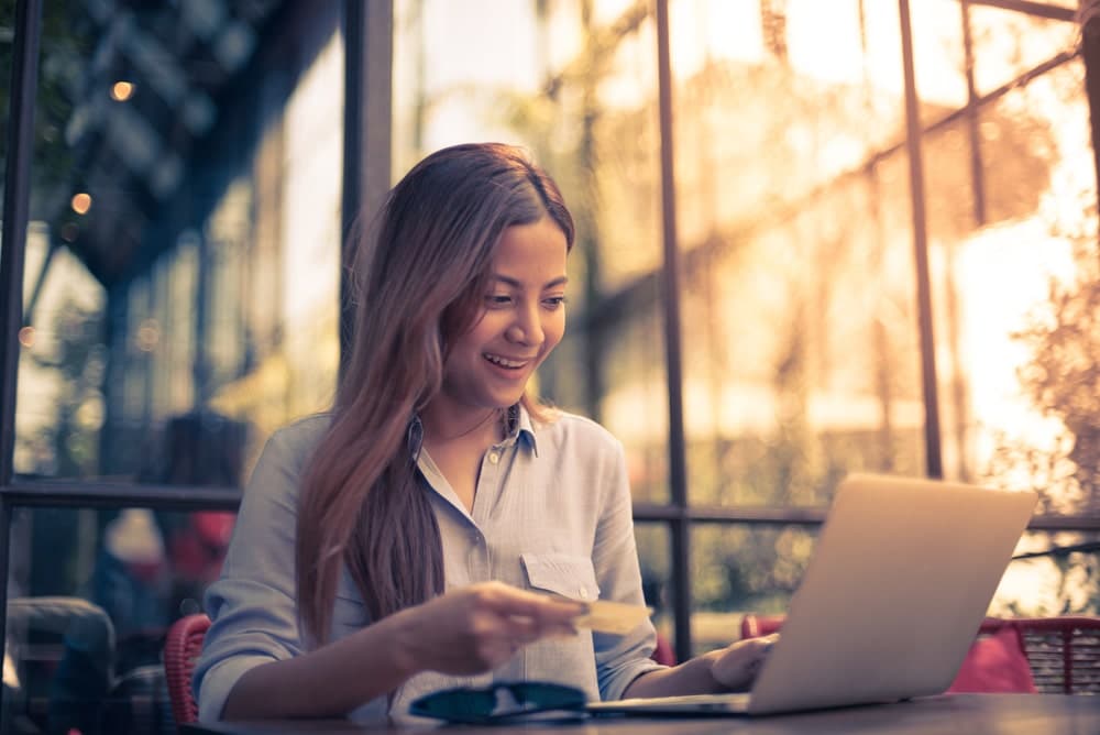 Health Insurance Banner - A smiling woman sitting in a cafe on her laptop