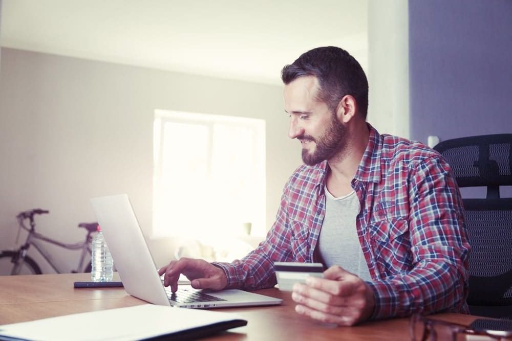 Man looking at his laptop at a table while holding a credit card