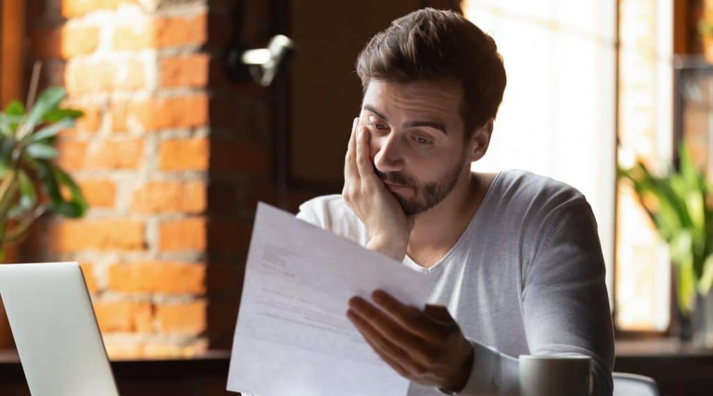 A man looking stressed and overwhelmed staring at his bank statements