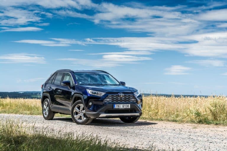 Car Insurance Banner - Black 4X4 vehicle parked on a gravel road in front of grass overlooking the ocean.