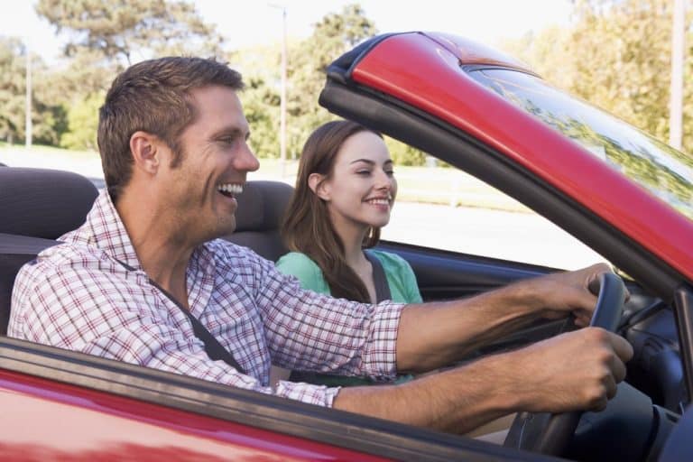 Car Insurance Banner - Happy couple driving an open-top red car.