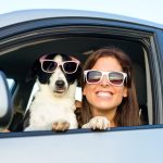 Pet Insurance Banner - Woman sitting in the car smiling with her dog, both wearing sunglasses