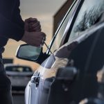 Thief breaking into a car at dusk in a car park