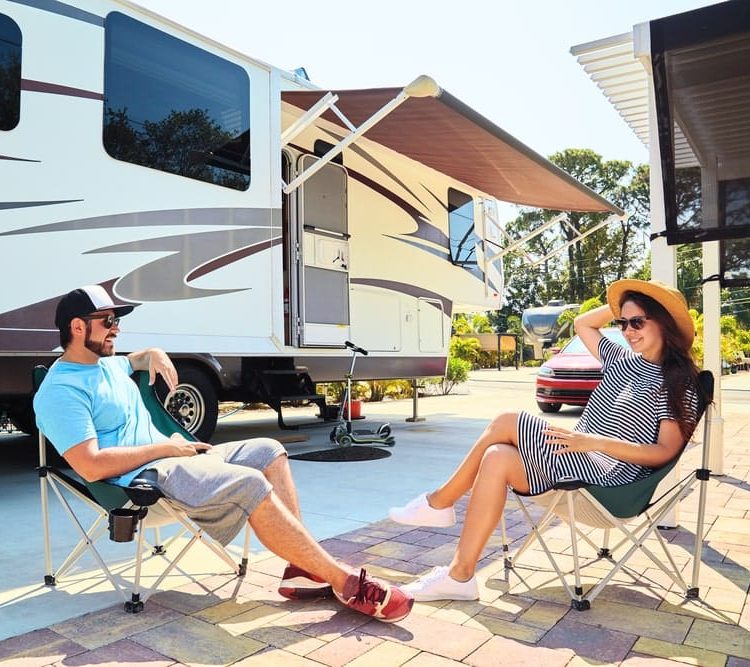 Caravan Loans Banner - Couple sitting on camper chairs outside their caravan in a caravan park