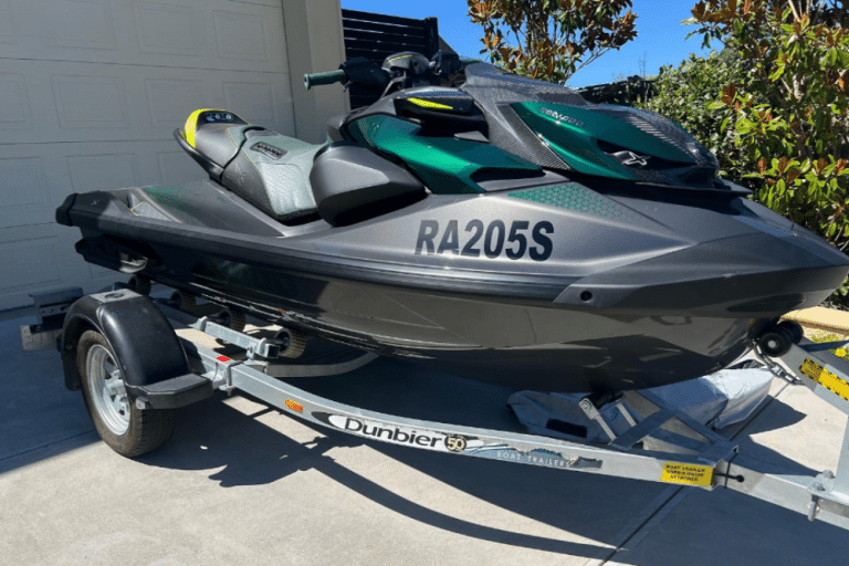 Green second hand Jet Ski parked on trailer in driveway.