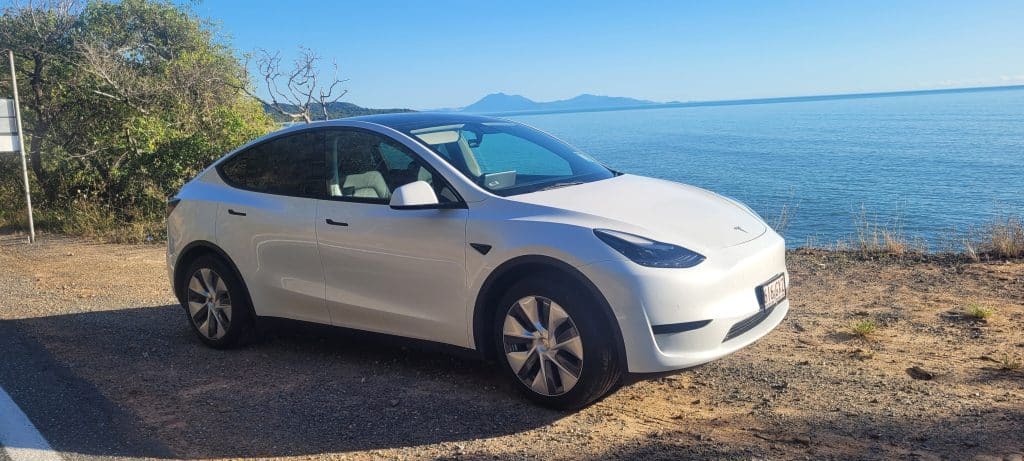 A white Tesla Model Y, parked beside the sea in far north Queensland, between Cairnes and Port Douglas