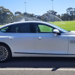 Matte White 2024 Genesis G80 electric car next to park.