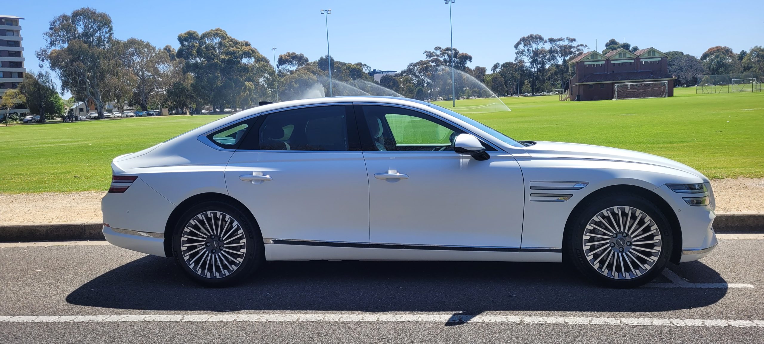 Matte White 2024 Genesis G80 electric car next to park.