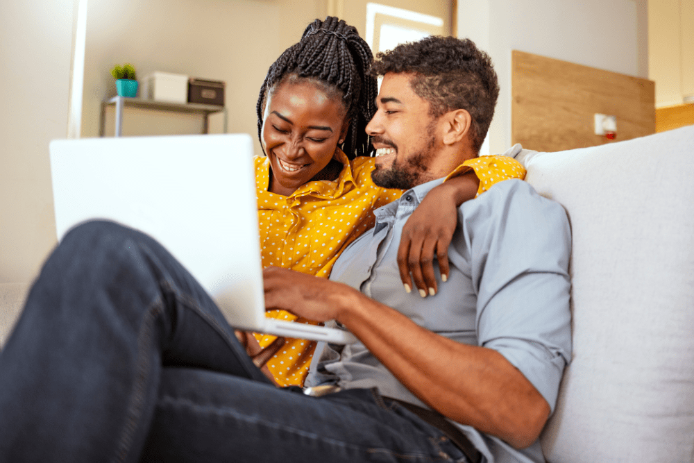 Couple smiling at their laptop while sitting on the couch