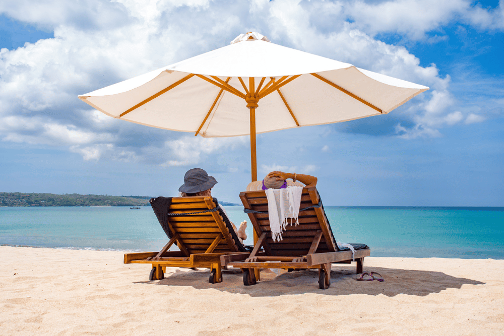 Couple sitting together in deck chairs on the beach under an umbrella