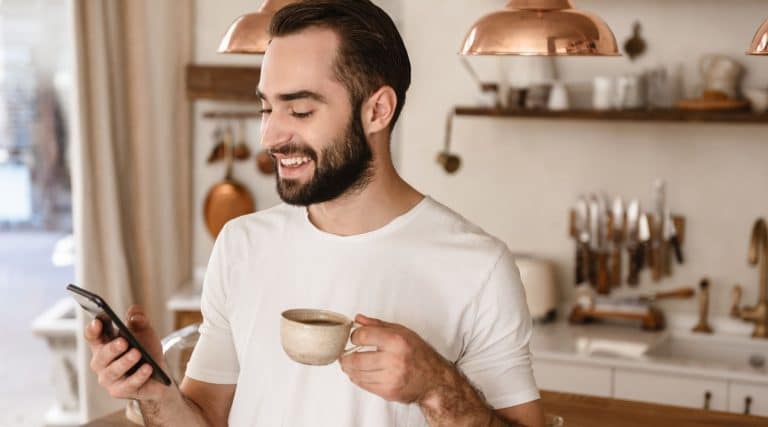 Man smiling at his phone while holding a mug of coffee