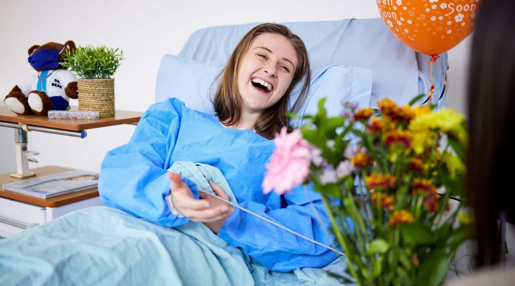 A woman in a hospital bed with get well gifts