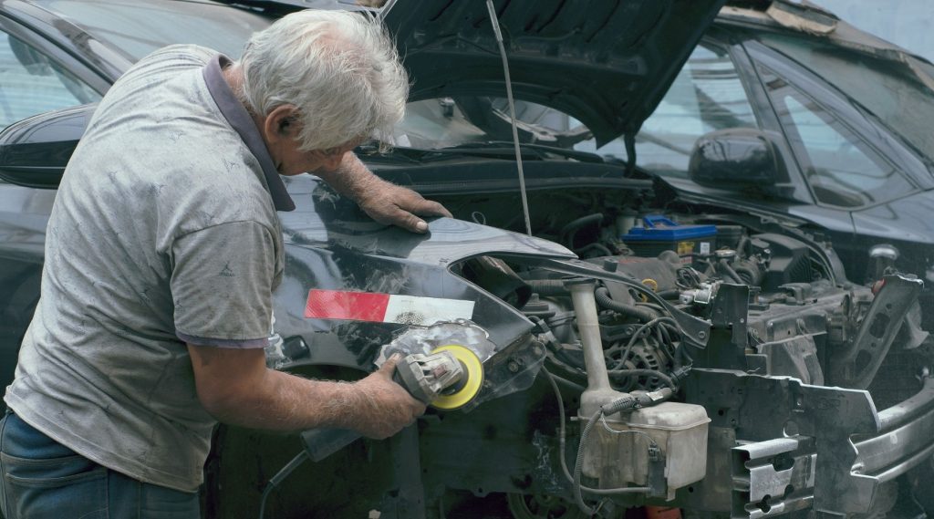 Older man repairing a car in a workshop