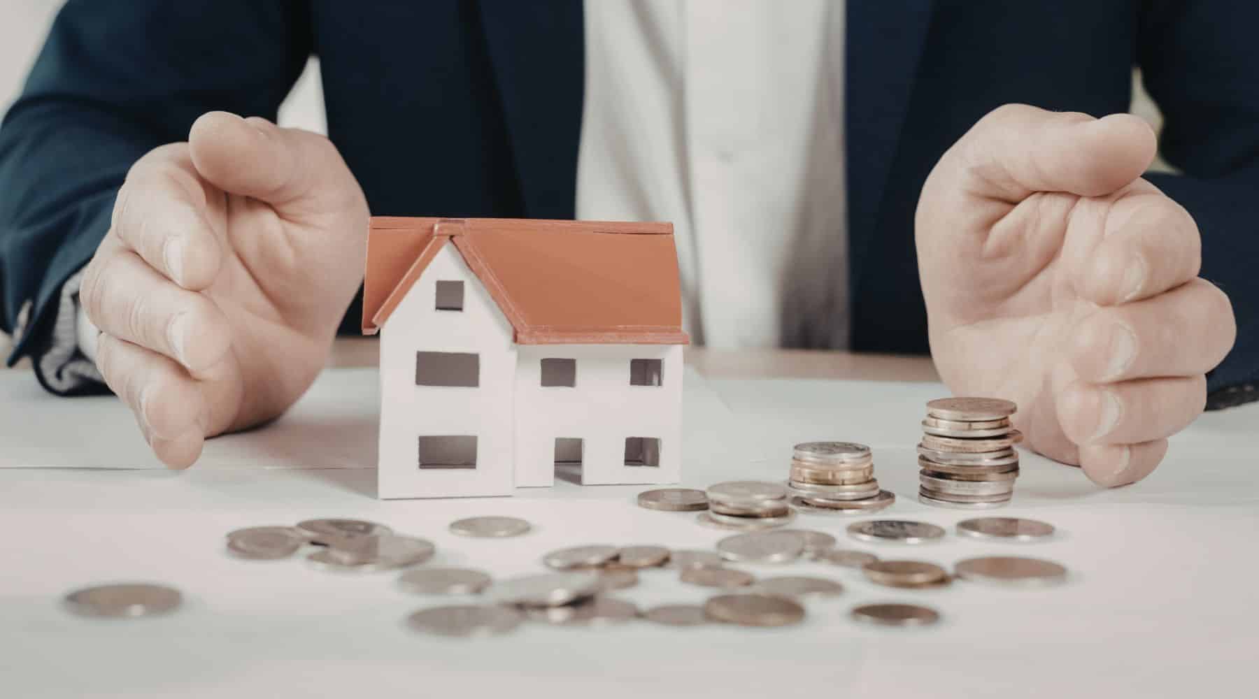 Man sitting in front of a miniature house with coins
