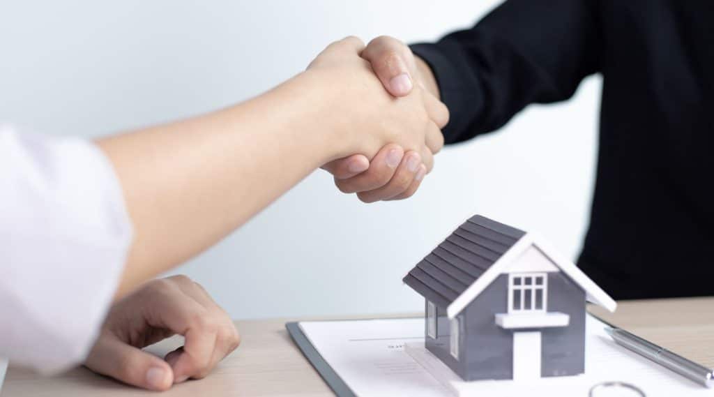 A buyer and home loan broker shaking hands next to house model.