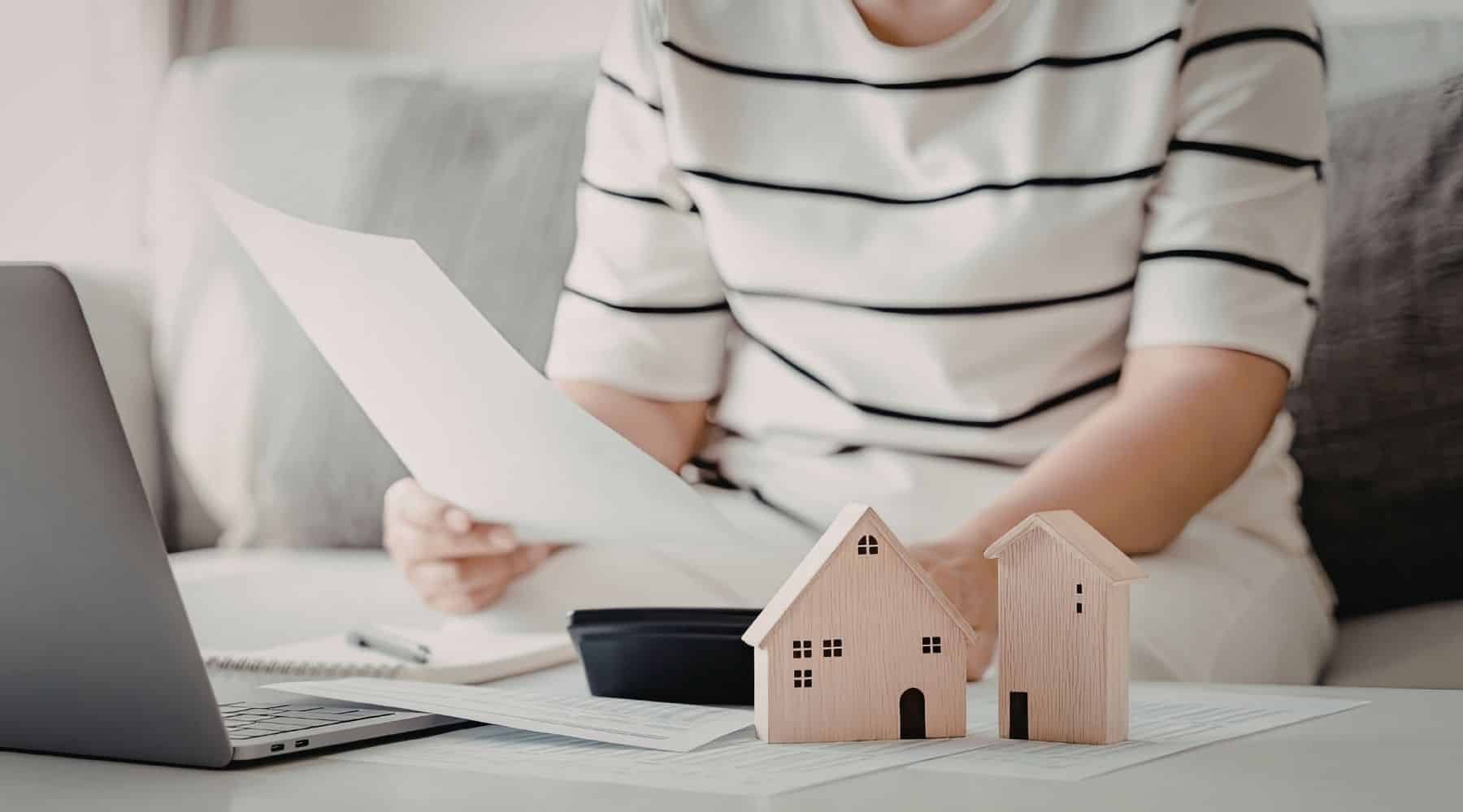 A person using a laptop and calculator next to model houses