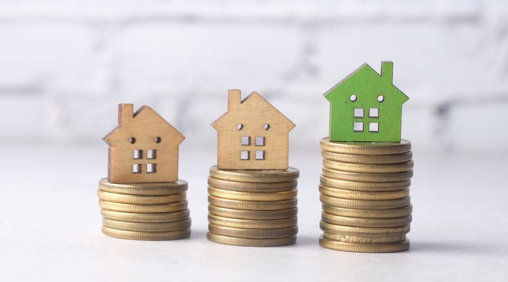 Small model houses sitting on stacks of gold coins