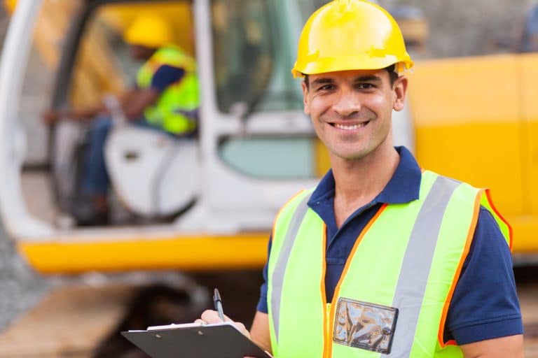 Man with hard hat standing in front of digger