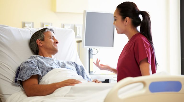 Man in a hospital bed talking to nurse