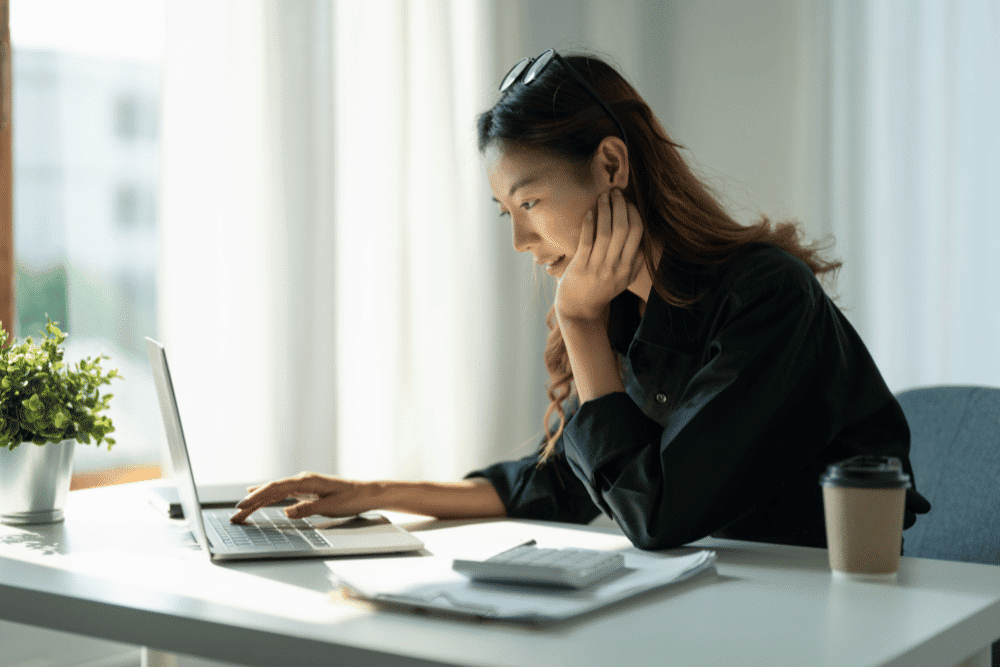 Businesswoman looking at laptop with a calculator on her desk