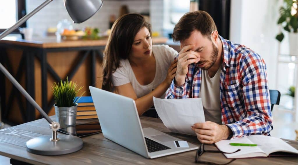 “A man holding papers next to his laptop, looking surprised and concerned.