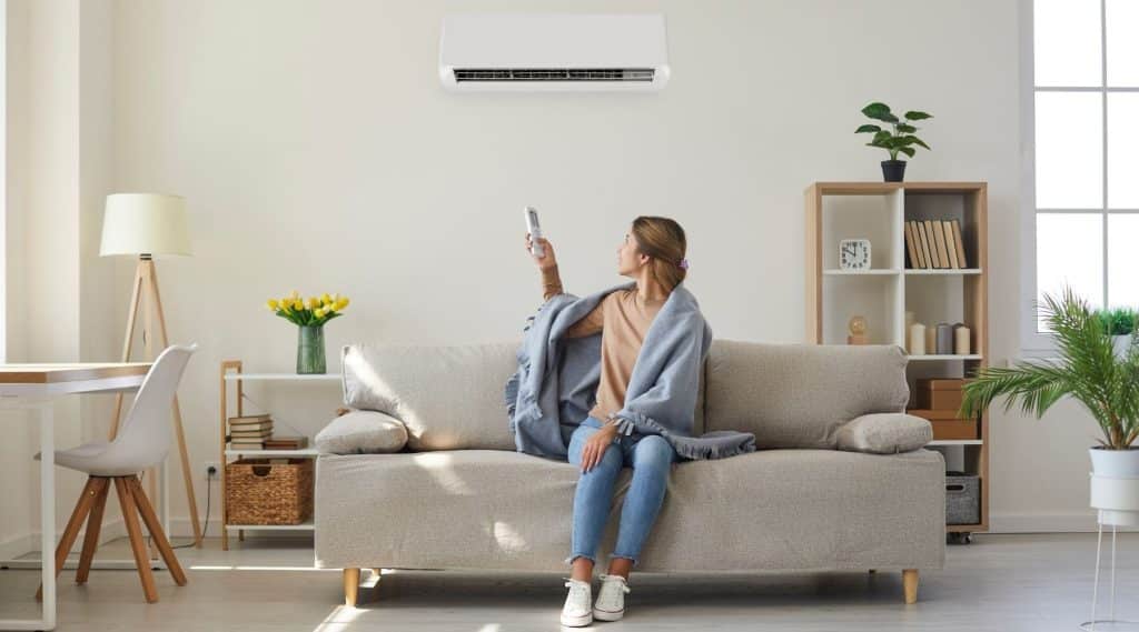 A woman sitting on her sofa turning on her AC unit.