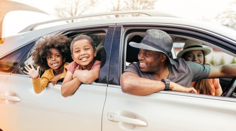 Family smiling out the car window before a road trip