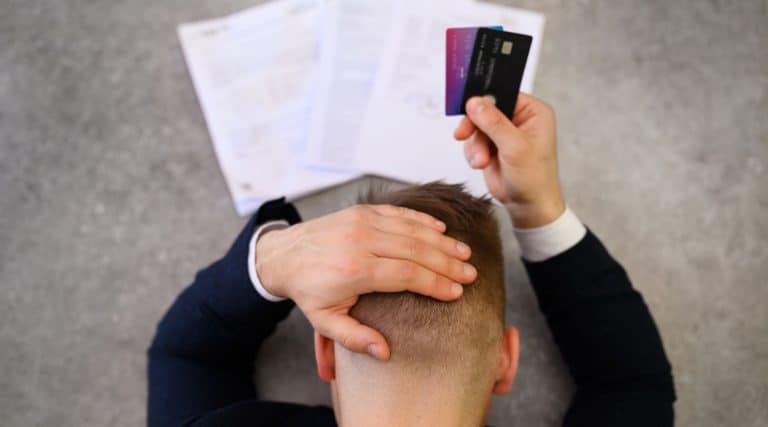 Man holding his head while looking at bills and holding credit cards