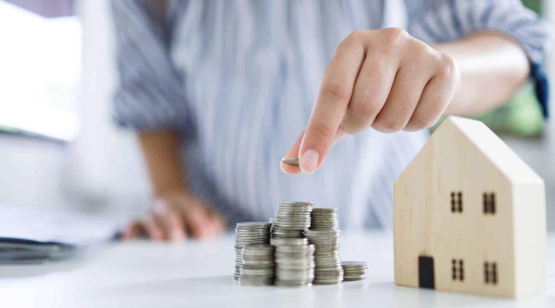 Woman piling coins next to a miniature house